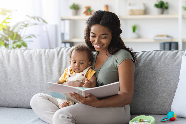 Muotokuva huolehtiva musta äiti käsittelyssä kirja pieni vauva kotona - Valokuva, kuva