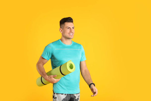 Handsome man with yoga mat on yellow background - 写真・画像