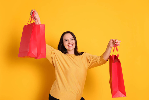 Beautiful overweight woman with shopping bags on yellow background - Foto, afbeelding