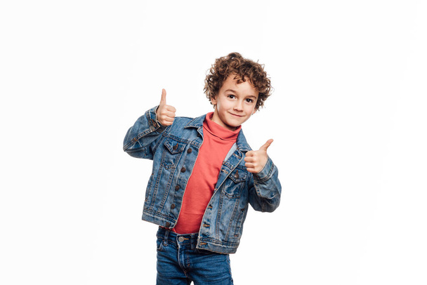 Young boy showing thumbs up while standing on an isolated white background. - Фото, изображение