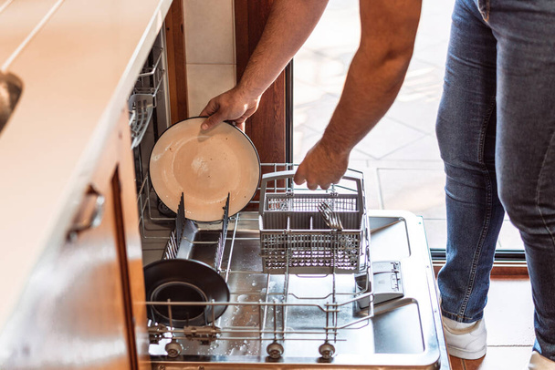 мужчина кладет грязную тарелку в посудомоечную машину - Фото, изображение