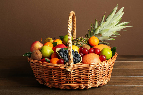 Assortment of fresh exotic fruits in wicker basket on wooden table - Zdjęcie, obraz