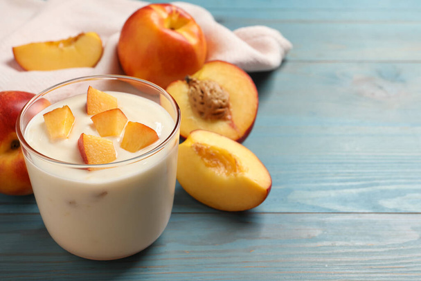 Tasty peach yogurt with pieces of fruit in glass on light blue wooden table, space for text - Фото, зображення