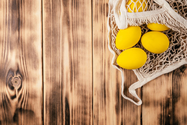 Composición de Pascua de la postal de celebración de saludo, fondo de madera de vacaciones y huevos de color amarillo en bolsa de cuerda - Foto, imagen