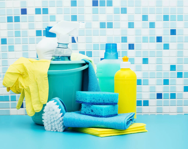 Limpiadores y detergentes en cubo, accesorios para la limpieza de diversas superficies y habitaciones de fondo azul - Foto, Imagen