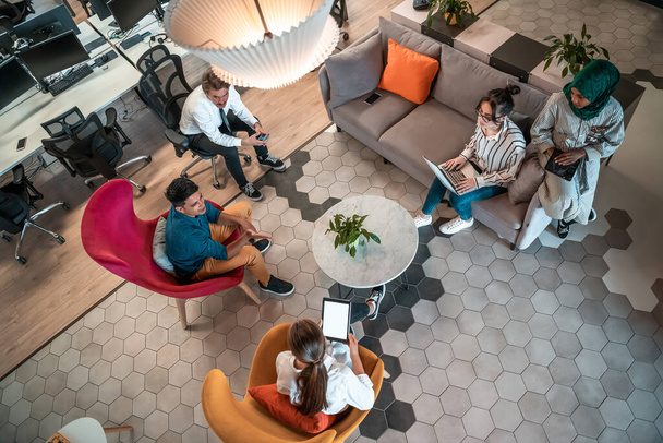 Top view photo of Multiethnic startup business team having brainstorming in relaxation area of modern office interior working on laptop and tablet computer. High-quality photo - Photo, image