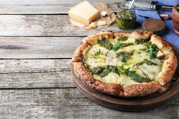 Delicious pizza with pesto, cheese and arugula on wooden table. Space for text - Фото, изображение