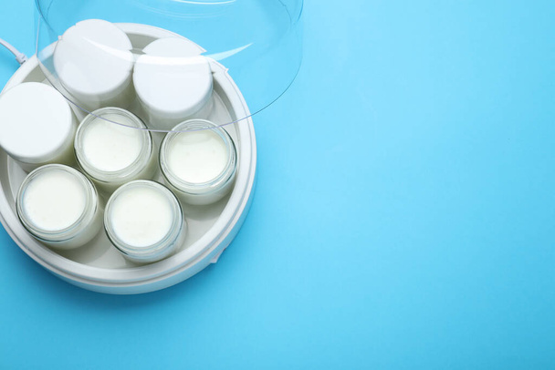 Modern yogurt maker with full jars on light blue background, top view. Space for text - Foto, afbeelding