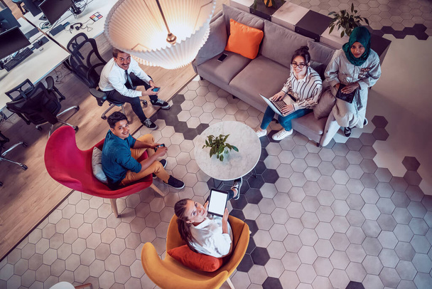 Top view photo of Multiethnic startup business team having brainstorming in relaxation area of modern office interior working on laptop and tablet computer. High-quality photo - 写真・画像