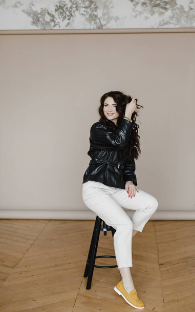 a beautiful curly-haired brunette girl in a leather jacket poses for an advertisement for luxurious hair - Valokuva, kuva