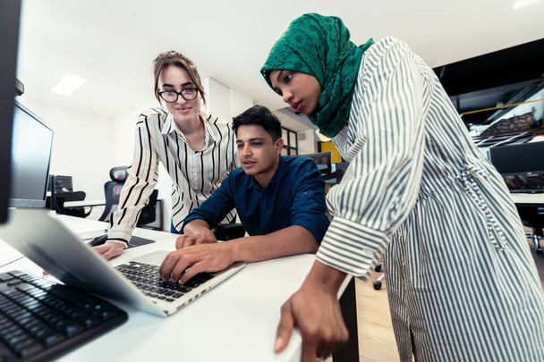 Πολυεθνική startup επιχειρηματική ομάδα Αραβική γυναίκα φορώντας μια μαντίλα στη συνάντηση στο σύγχρονο ανοιχτό σχέδιο γραφείο εσωτερικό brainstorming, εργάζονται σε φορητό υπολογιστή και επιτραπέζιο υπολογιστή. Επιλεκτική εστίαση. Υψηλής ποιότητας - Φωτογραφία, εικόνα