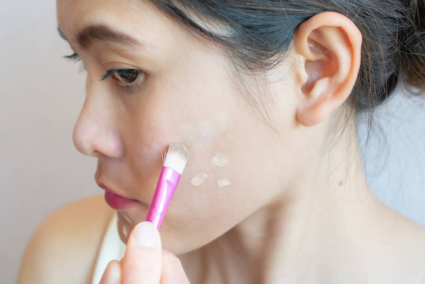 Retrato de mulher asiática aplicando corretor em sua pele facial com escova. Concealer é um tipo de cosmético que é usado para mascarar olheiras, manchas de idade, poros grandes etc. - Foto, Imagem