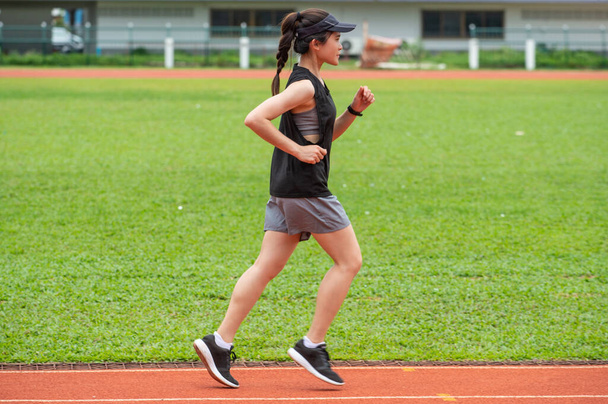 Вид сбоку молодой спортсменки бегущей по беговой дорожке на стадионе. Беговая дорожка - это резиновая искусственная беговая дорожка для легкой атлетики. - Фото, изображение