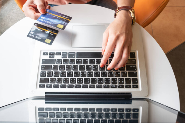 オンラインショッピングのためのラップトップを使用している間にクレジットカードを保持する誰かのトップビュー。オンラインショッピングは、インターネット上の商人から商品やサービスを購入するプロセスです。. - 写真・画像