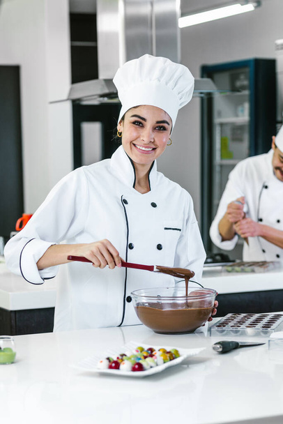 latin woman pastry chef wearing uniform holding a bowl preparing delicious sweets chocolates at kitchen in Mexico Latin America - Foto, Bild