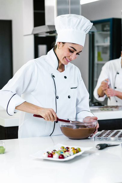 latin woman pastry chef wearing uniform holding a bowl preparing delicious sweets chocolates at kitchen in Mexico Latin America - Fotografie, Obrázek