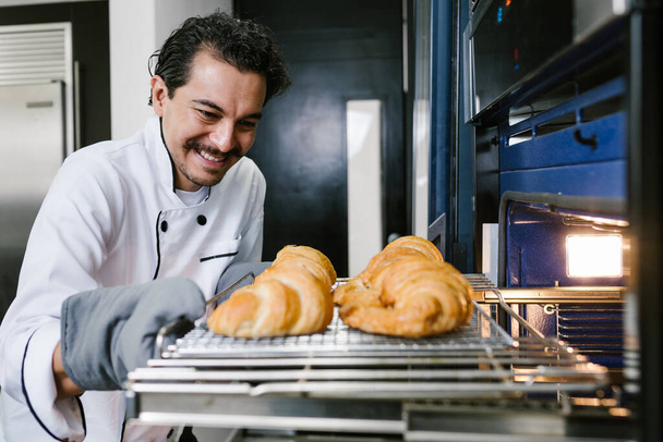 молодой латиноамериканец пекарь и выпечка круассанов и хлеб на духовке на кухне в Мексике Латинская Америка - Фото, изображение