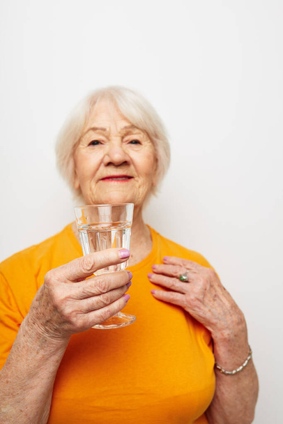 Cheerful elderly woman holding a glass of water health light background - Fotó, kép