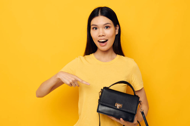 Portrait Asian beautiful young woman with a black womans bag in her hands yellow background unaltered - Φωτογραφία, εικόνα