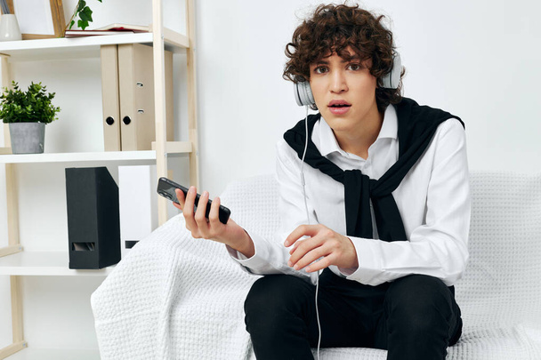 blogger en auriculares sentados en un sofá blanco sala de estar del teléfono inteligente - Foto, Imagen