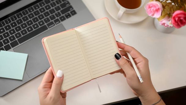 Top view of open school notebook with blank pages in women's hands over modern office desk. Feminine workspace - Φωτογραφία, εικόνα