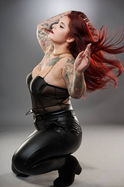 Glamour plus size model covered in tattoos in lingerie and leather on gray background - Foto, Imagem