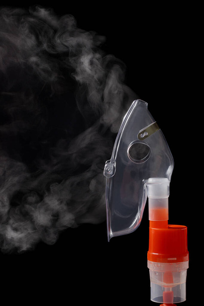 Průhledná respirační maska na rozprašovacím kelímku s párou na černém pozadí. Kyslíkový sprej inhalátor pro astma a respirační onemocnění. - Fotografie, Obrázek