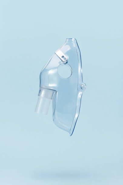 Transparent respiratory mask for compressor nebulizer flying on blue background. Medical equipment for inhalation therapy for asthma and respiratory diseases. - Photo, image