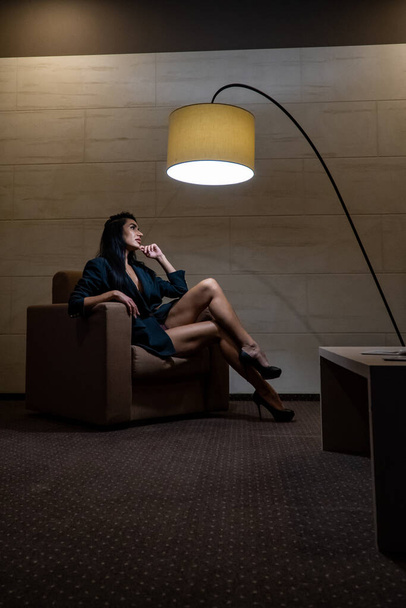 красивая молодая женщина в черной куртке позирует в кресле в комнате - Фото, изображение