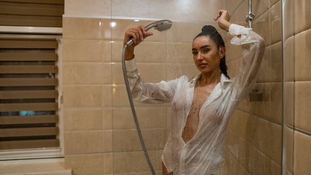 Güzel, genç bir kadın banyoda poz veren tek bir ıslak erkek gömleğiyle çıplak. - Fotoğraf, Görsel