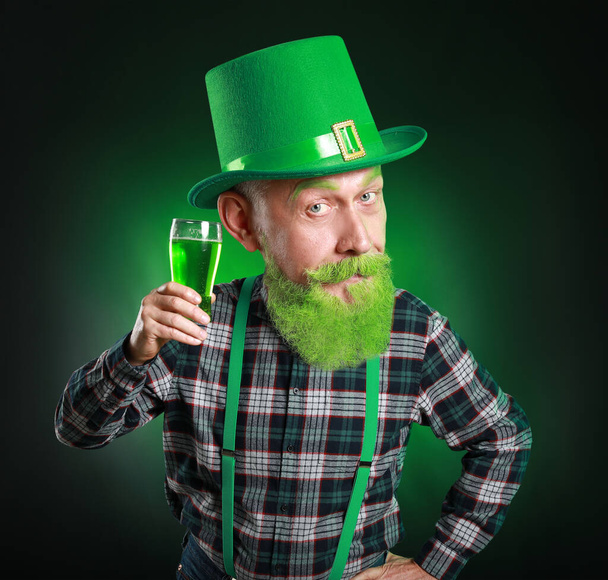 Hombre maduro divertido con cabeza grande y vaso de cerveza sobre fondo verde oscuro. Celebración del Día de San Patricio - Foto, imagen