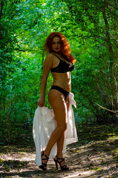 beautiful young woman in a black lingerie posing in green summer forest  - Фото, зображення