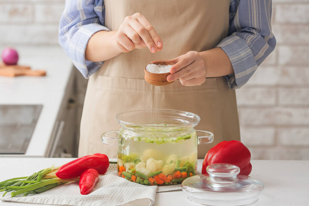 Woman adding salt in tasty dietary soup on table in kitchen - Foto, immagini