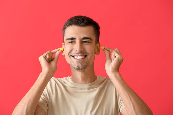 Χαμογελώντας νεαρός άνδρας βάζοντας ωτοασπίδες σε κόκκινο φόντο - Φωτογραφία, εικόνα