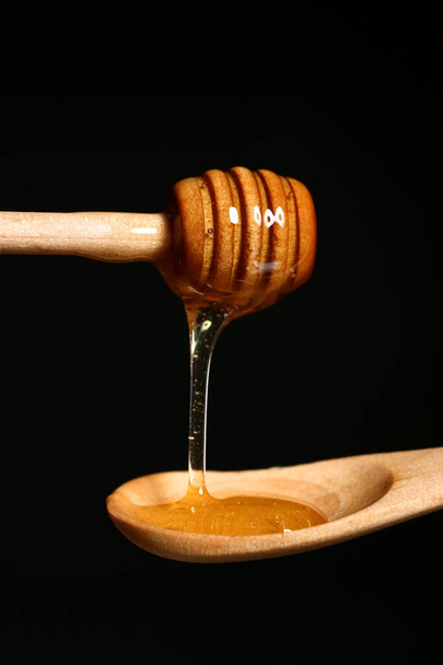 蜂蜜は黒を背景に木製のスプーンにディップから滴下,クローズアップ - 写真・画像