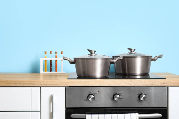Metal cooking pots on stove and spices on wooden table near color wall - Photo, Image