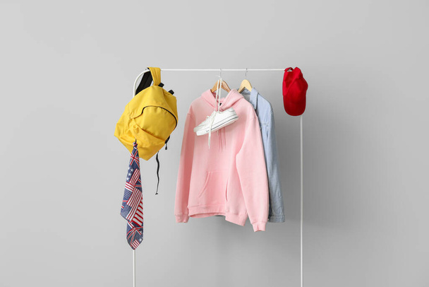Rack with stylish clothes, backpack, sneakers and cap near light wall - Zdjęcie, obraz
