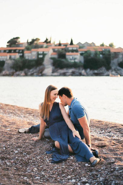 Ο άντρας φιλάει τη γυναίκα στον ώμο στην παραλία με θέα το νησί Σβέτι Στεφάν. Μαυροβούνιο - Φωτογραφία, εικόνα