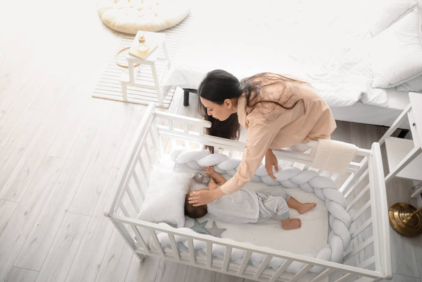 Young mother and her adorable baby sleeping in crib at home - Photo, image