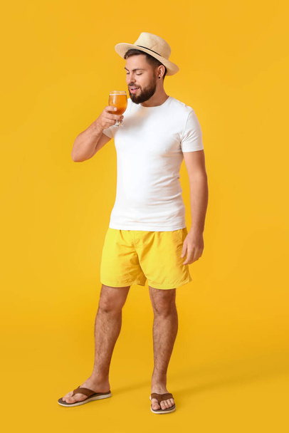 Joven con sombrero bebiendo cerveza sobre fondo amarillo - Foto, Imagen
