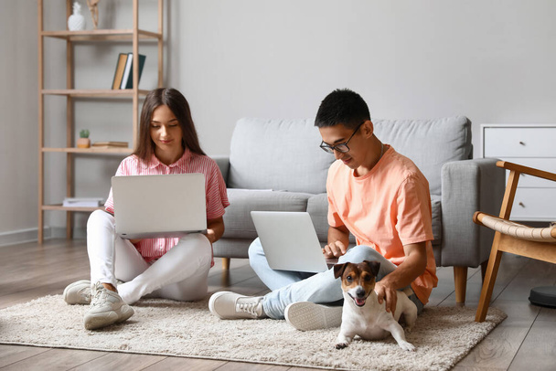 Νεαρό ζευγάρι με χαριτωμένο σκυλί χρησιμοποιώντας φορητούς υπολογιστές στο πάτωμα στο σπίτι - Φωτογραφία, εικόνα