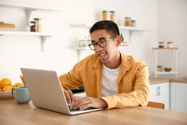 Fiatal ember használ laptop konyha asztalnál - Fotó, kép
