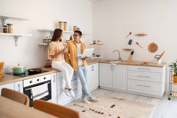 Young woman with cup of coffee and her husband holding laptop in kitchen - Foto, Bild