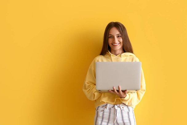 Pretty young woman with laptop on yellow background - Foto, Imagen