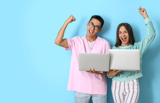 Ευτυχισμένο νεαρό ζευγάρι με φορητούς υπολογιστές σε μπλε φόντο - Φωτογραφία, εικόνα