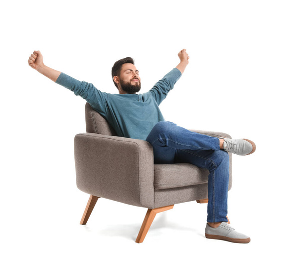 Handsome bearded man stretching in grey armchair on white background - Фото, зображення
