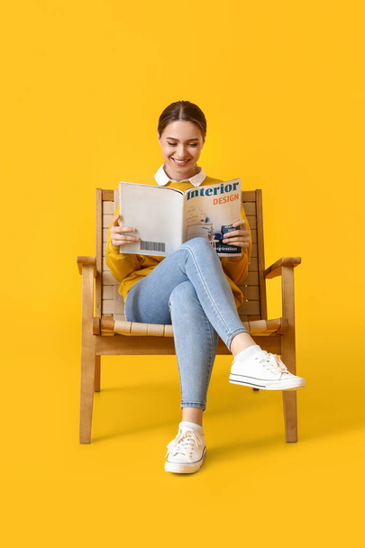 Beautiful woman reading magazine in wooden armchair on yellow background - Фото, зображення
