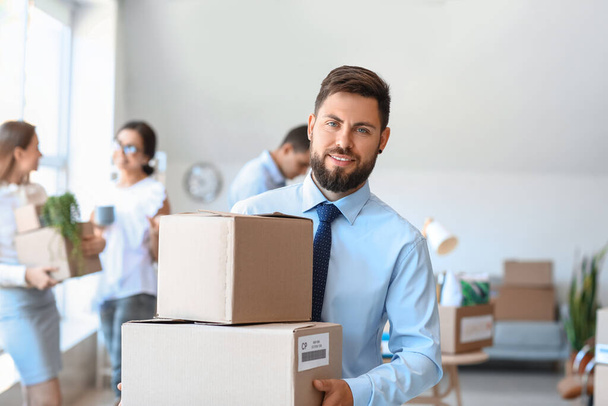 Handsome man holding boxes with things in office on moving day - Foto, Bild