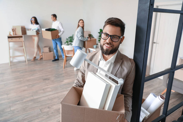 Handsome man holding box with personal things in office on moving day - Photo, Image