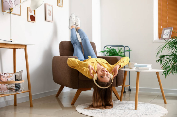 Mujer joven y bonita con auriculares tumbados en un sillón suave en casa - Foto, Imagen